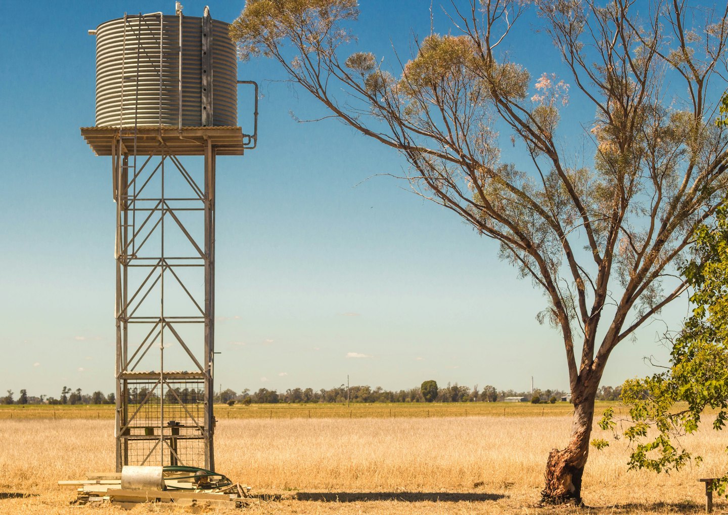 Galvanized water tank on a truss stand in a dry field.