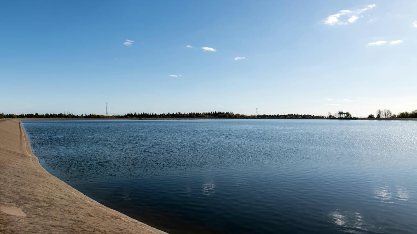 Blue reservoir with concrete embankment and distant industrial structures.