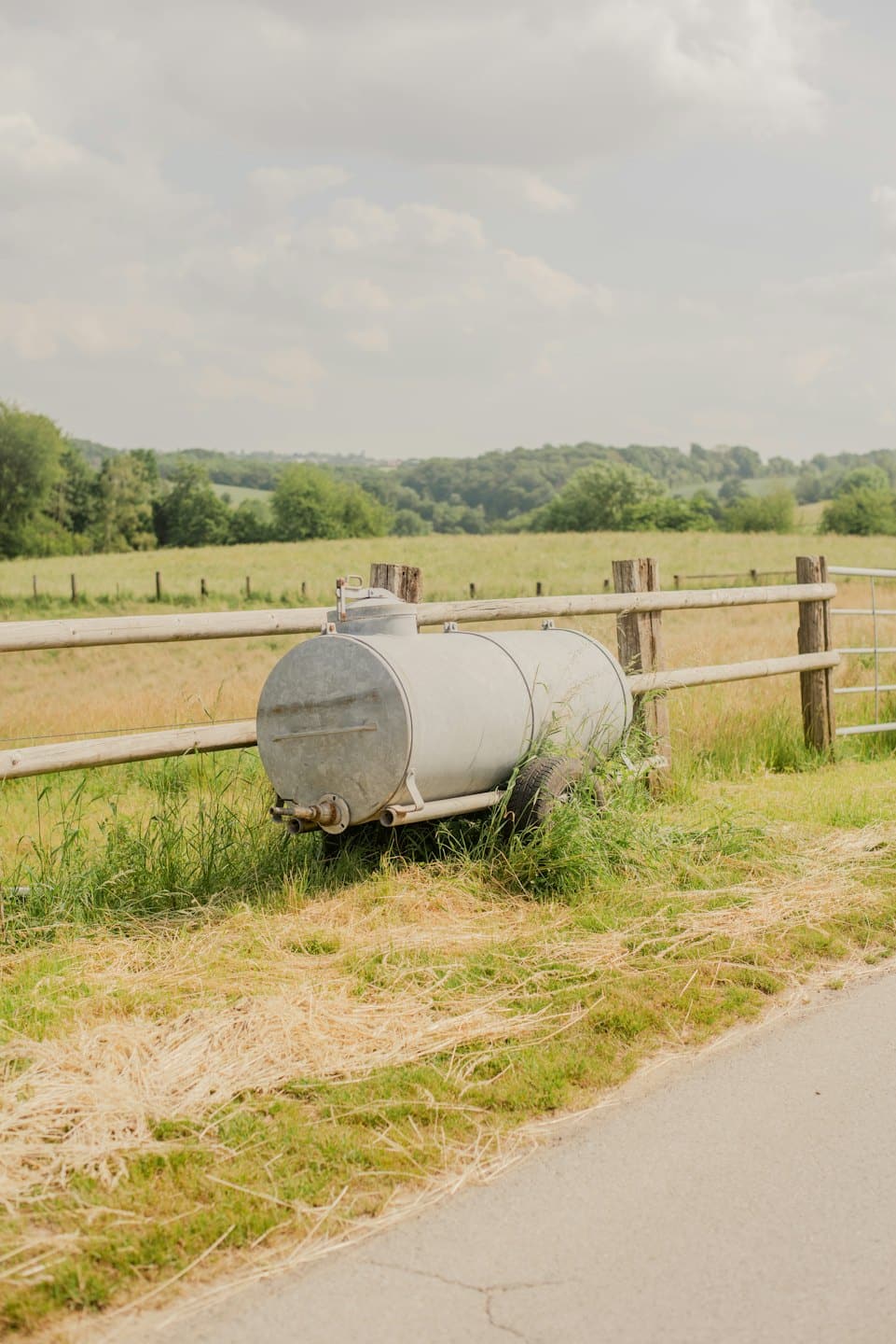 Metal water tank on a trailer beside a wooden fence.